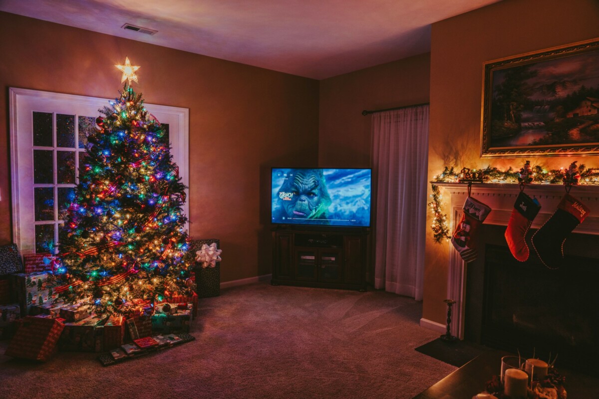 Cozy living room with a decorated Christmas tree, gifts, stockings on the fireplace, and a TV showing a screen cap of "How the Grinch Stole Christmas"