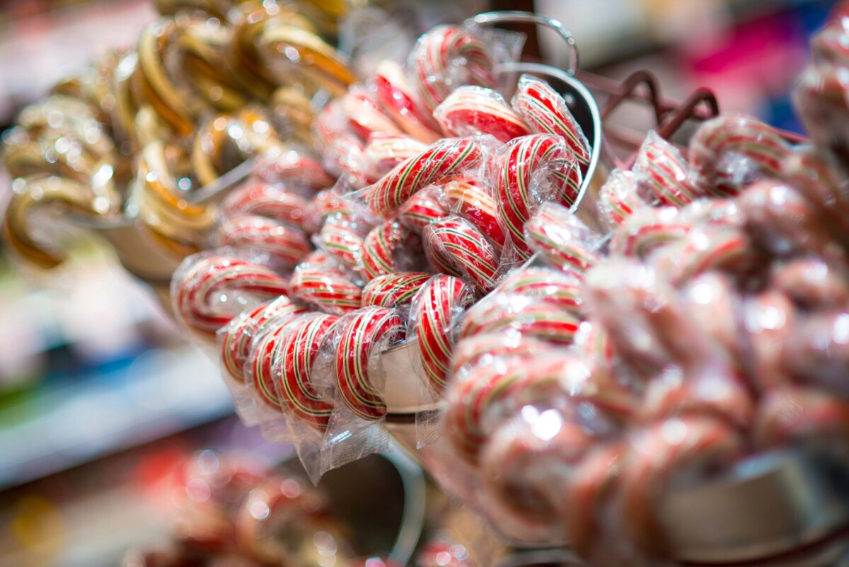 A close-up of red, green, and white striped candy canes wrapped in clear plastic sit in three silver tin containers.
