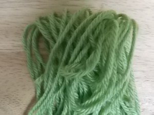 a pile of green commercial acrylic yarn resting on a wooden background