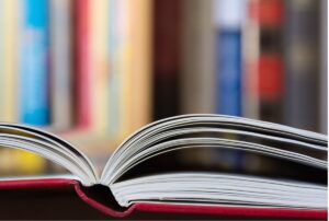 An open book viewed from the top of its spine; more books are visible shelved in the background