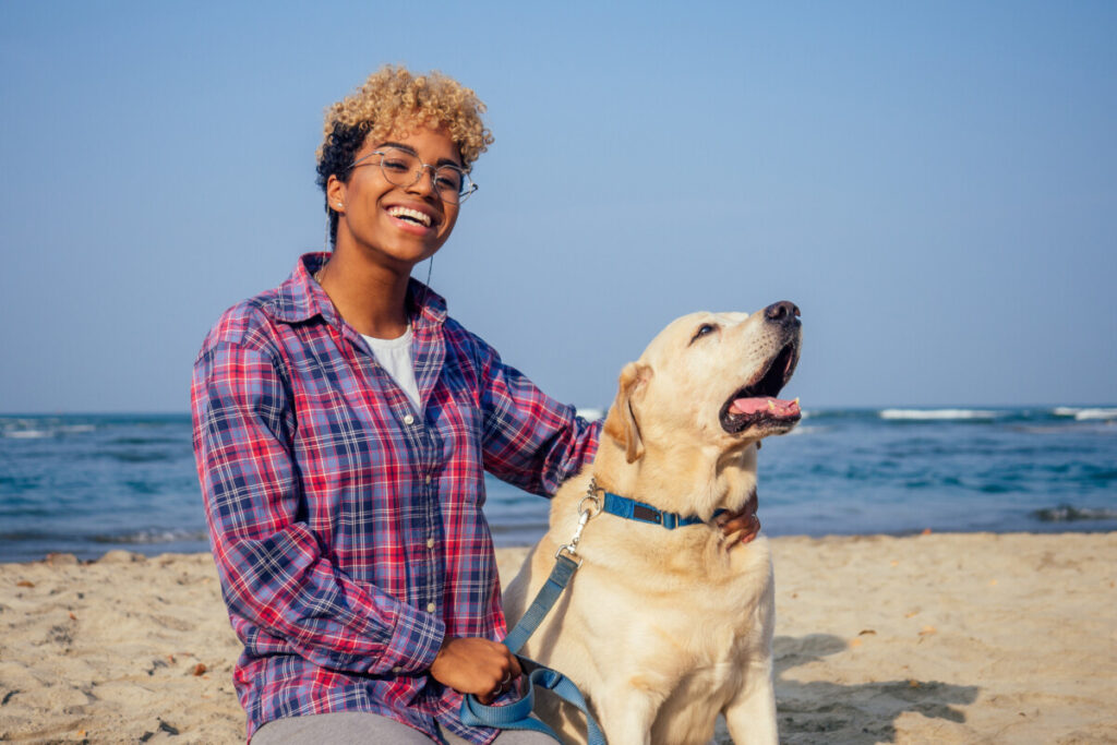 Woman sitting next to a dog on a beach and looking content