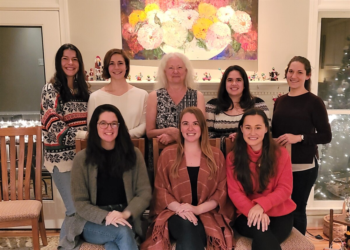 A photo of the lab members smiling in front of a mantle. Lucy, Julia, Dr. Bauer, Dr. Miller-Goldwater, and Dr. Dugan stand, while Alissa, Katie, and Melanie sit in front of them.