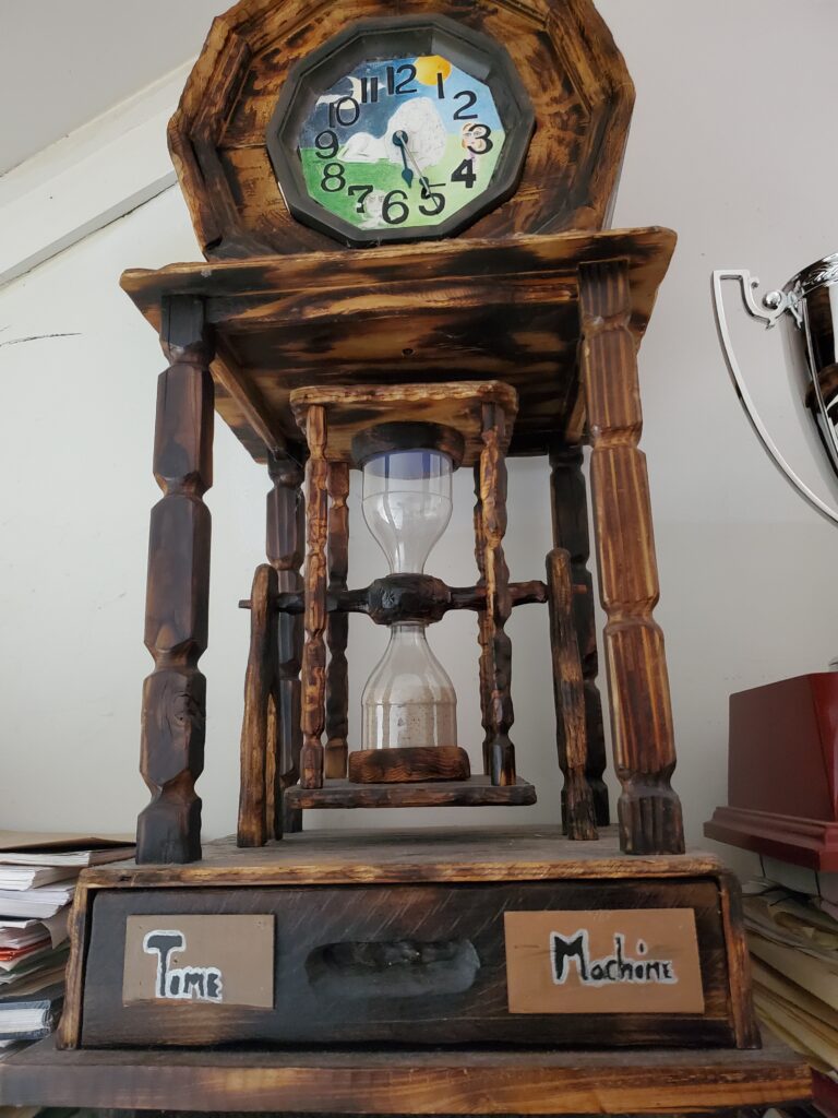 Handmade wooden hourglass featuring hand-painted clock and plaque with words Time Machine.