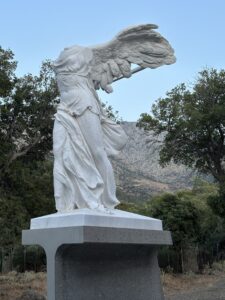 A photo of the Winged Victory of Samothrace on a dark gray pedestal with mountains in the background