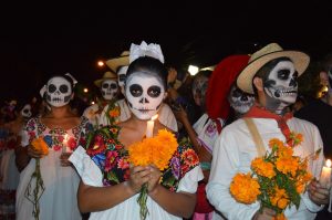 Individuals in Mexico, with painted faces as skulls and holding marigolds, walk together during this holiday to honor and celebrate their loved ones who have passed. 