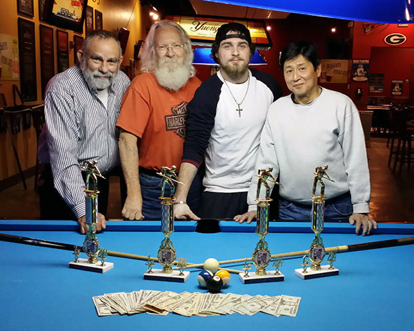 Photo of four men standing behind a pool table