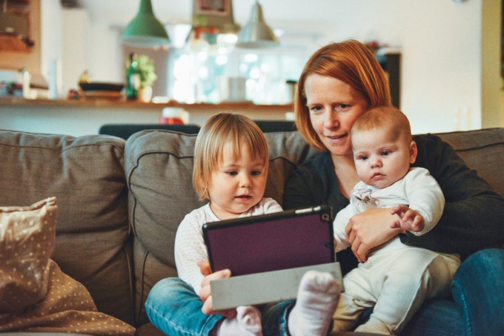 A mother and two young children look at an iPad together on a sofa