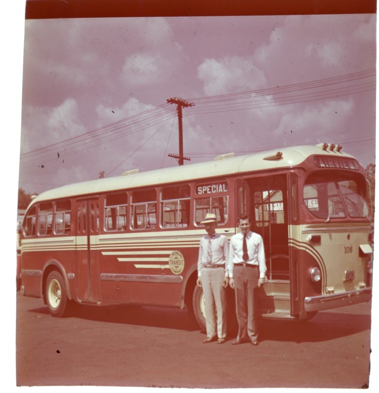 One black man and one white man stand in front of a bus, circa 1940.