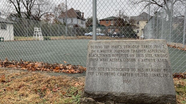 Tennis court in background with stone memorial marker in front.