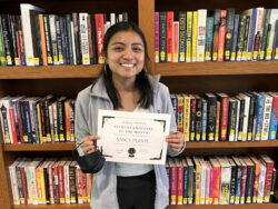 Nancy Puente with her certificate in front of the book stacks.