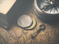 Image of old map with a vintage compass, keys, and book corner.