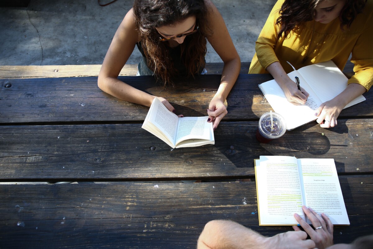Young people with open books at a wooden picnic table