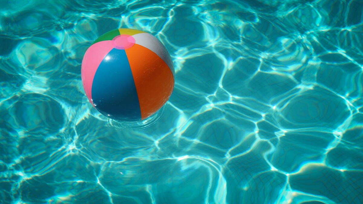 A plastic, multicolored beach ball floats in a pool.