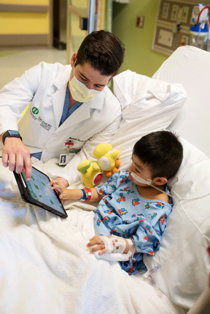 A doctor and pediatric patient use the nurse communication tool on a tablet in a hospital room
