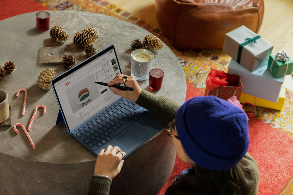 A person in a blue beanie uses a stylus on a laptop for their holiday shopping