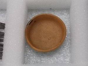 A small reddish bowl made of clay resting in a foam partition inside one of the cardboard boxes