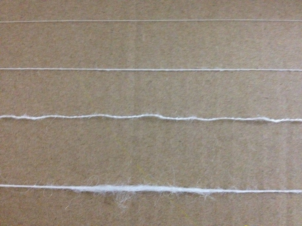 The top thread is commercially made, the middle thread is my own thread on a good day, the third is my thread plyed (I'll get to that in the next post) and the last is my thread on a bad day. All the threads are white and rest against a cardboard back ground