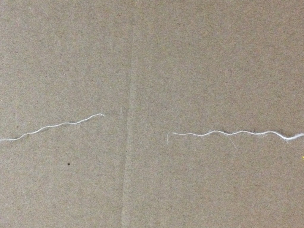 This is a photo of a piece of thread I have spun which broke in half. Each half is twisting away from the other and the ends are frayed. The background is the cardboard that I have used to shoot all the spining photos.