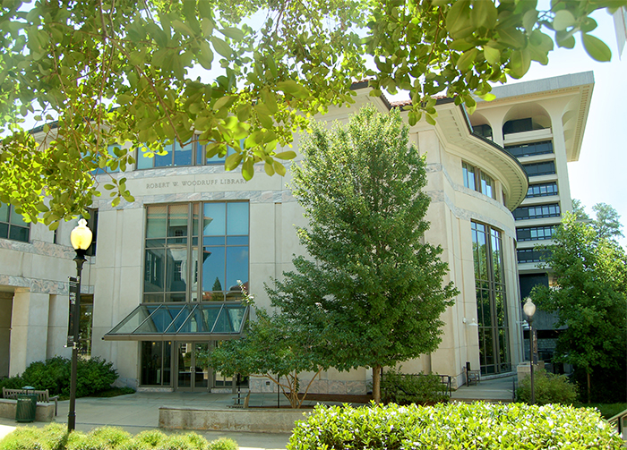 Image of the front exterior of Woodruff Library entrance with green-leafed trees, partially showing the stack tower behind entrance section of the building.